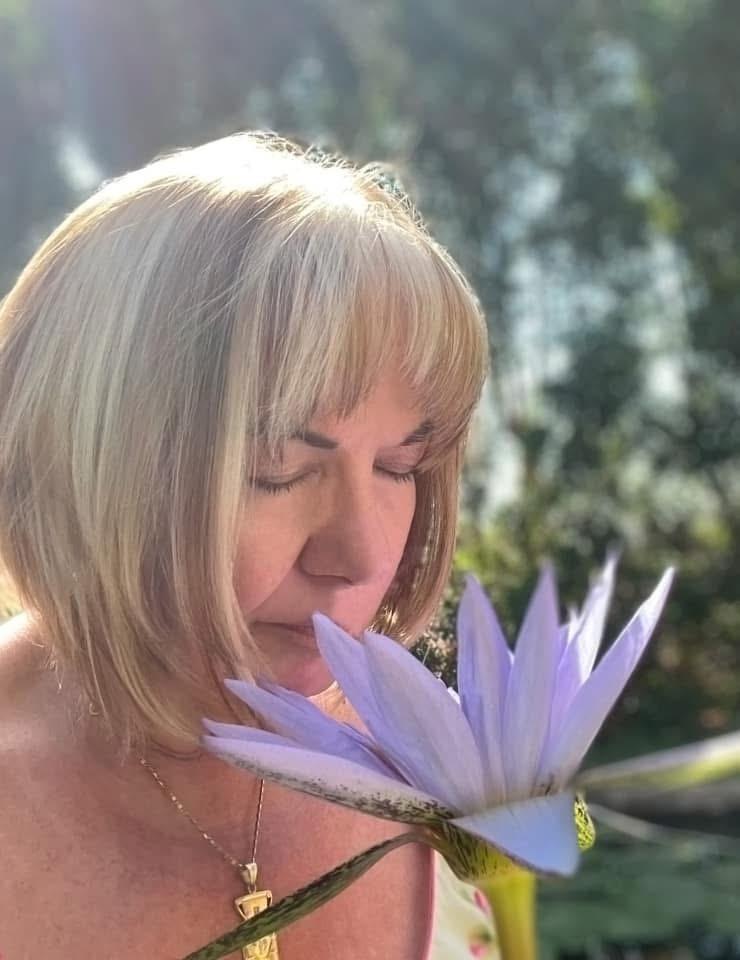 Mary Lomando holding a blue lotus to her face, the bloom as wide as her face